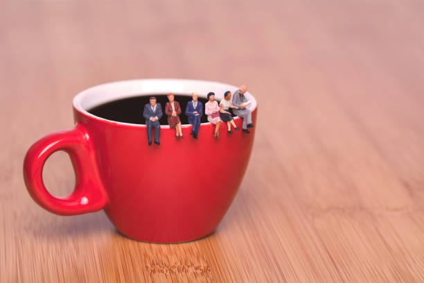 Creative concept about drinking coffee and waiting. Miniature people sit on the edge of a cup of coffee tea coffee break. Red cup on a wooden background. stock photo
