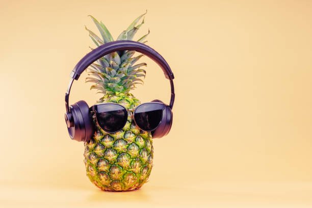 Creative idea of a pineapple image of a person headphones and glasses as a relaxing tourist on vacation. On a yellow background. stock photo