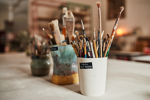 Creative paintbrush tools, equipment or objects for colorful and modern artwork, design and painting in an art studio or workshop. Jar or container of many different paint brushes in an empty room