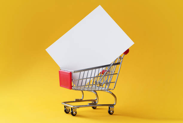 Creative shopping background with shopping cart and empty card in it on yellow background with copy space. stock photo