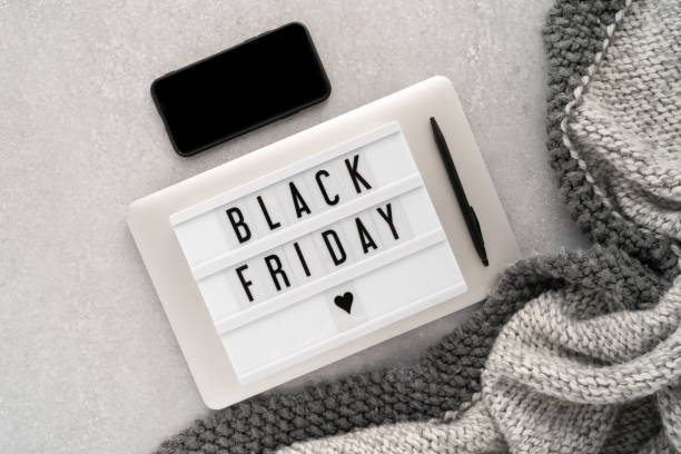 Creative top view flat lay promotion composition with text Black Friday on white Lightbox laying on grey laptop with black phone stock photo