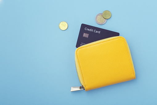 Credit card in wallet with coins on blue background, flatlay with copy space
