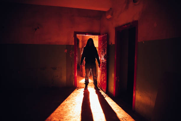 Creepy silhouette with knife in the dark red illuminated abandoned building. Horror about maniac concept stock photo