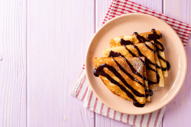 Crepes with chocolate syrup on purple wooden background. stock photo