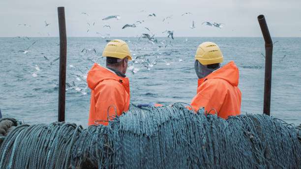 crew of fishermen work on commercial fishing ship that pulls trawl net. - fisherman imagens e fotografias de stock