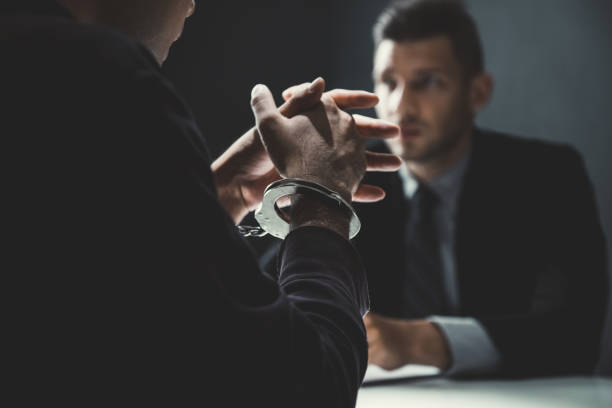 Criminal man with handcuffs being interviewed in interrogation room stock photo