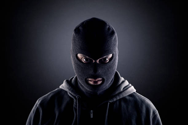 Criminal wearing black balaclava and hoodie in the dark stock photo