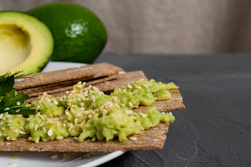 Crispbreads with mashed avocado sprinkled sesame seed on plate