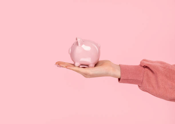Crop hand with piggy bank Hand of anonymous woman demonstrating small piggy bank on pink background coin bank stock pictures, royalty-free photos & images