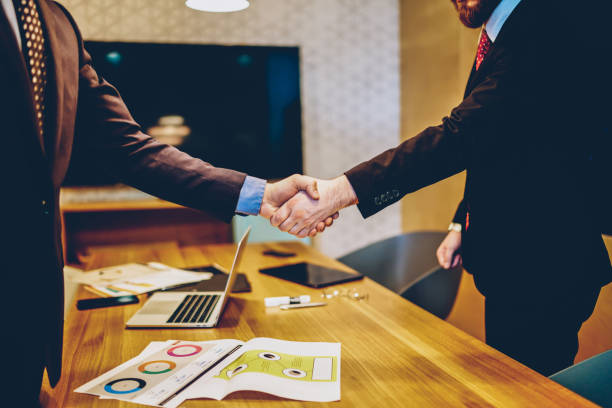 Cropped image of men in suits shaking hands making deal of sponsorship in business corporation, male entrepreneurs agree in partnership cooperation and contract during formal meeting in office stock photo