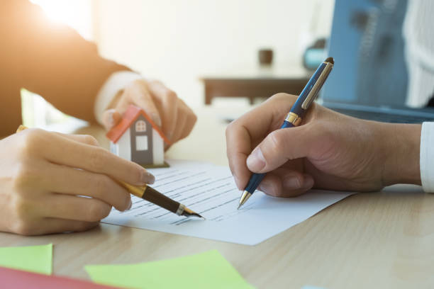 Cropped image of real estate agent assisting client to sign contract paper at desk with house model stock photo
