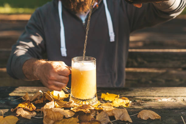 imagen recortada del joven vertiendo cerveza fresca en un vaso de cerveza, celebración de las fiestas de otoño y concepto de oktoberfest - mano agarrando botella de cerveza y taza fotografías e imágenes de stock