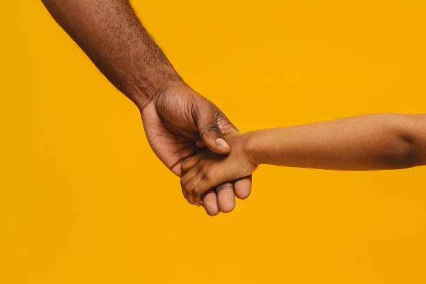 Cropped of african father and daughter holding hands Cropped of black father and daughter holding hands over yellow studio background african american children stock pictures, royalty-free photos & images