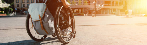 cropped panoramic view of man using wheelchair with bag on street with sunlight - wheelchair street imagens e fotografias de stock