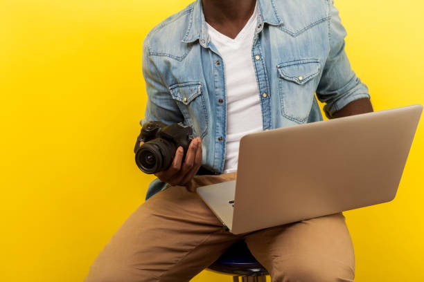 retrato recortado de fotógrafo masculino sosteniendo cámara digital dslr y portátil. aislado sobre fondo amarillo - video editing fotografías e imágenes de stock