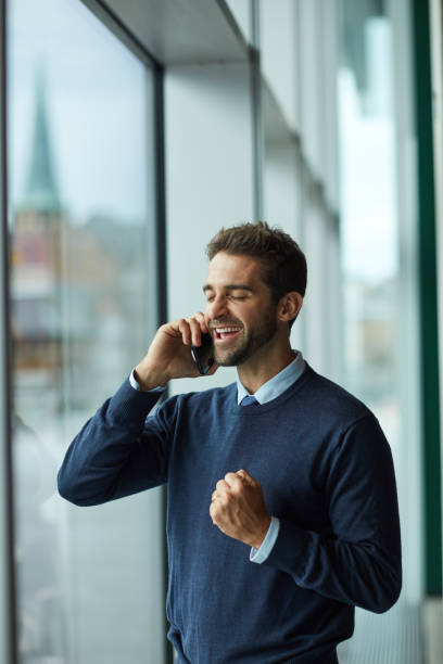 Cropped shot of a handsome young businessman standing indoors alone and using his cellphone stock photo
