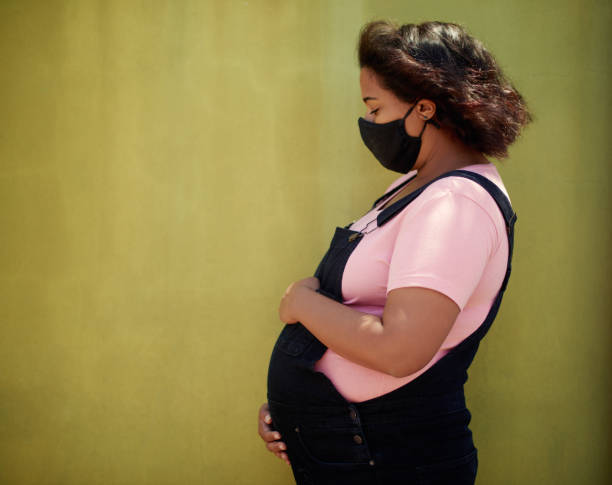 Cropped shot of an attractive young pregnant woman wearing a mask while posing against a gold background stock photo
