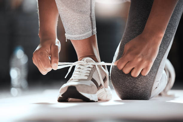 Cropped shot of an unrecognizable woman tying her shoelaces while exercising at the gym stock photo