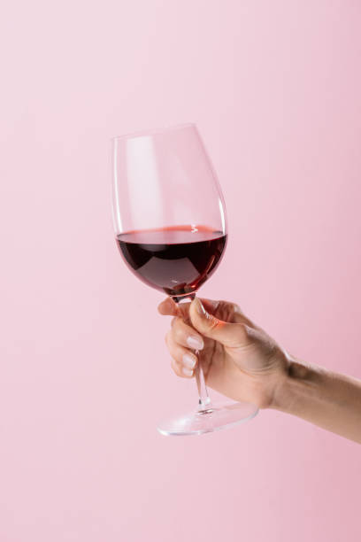 ภาพครอปของผู้หญิงถือแก้วไวน์แดงที่แยกได้บนสีชมพู - ไวน์ เครื่องดื่มแอลกอฮอล์ ภาพสต็อก ภาพถ่ายและรูปภาพปลอดค่าลิขสิทธิ์