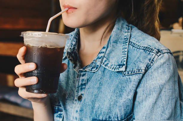Cropped shot view of woman drinking Iced coffee/cold drink in the cafe. Shot of woman drinking iced black coffee. black coffee stock pictures, royalty-free photos & images