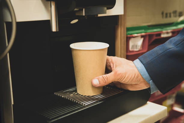cropped view of businessman pushing button on coffeemaker while preparing coffee to go. man takes coffee from a vending machine stock photo