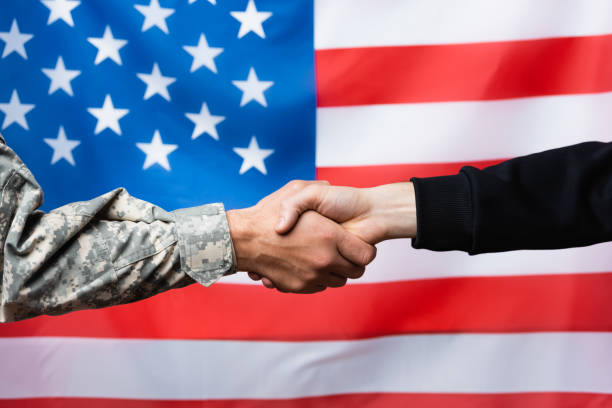 cropped view of soldier shaking hand with civilian man near american flag on blurred background  military to civilian  stock pictures, royalty-free photos & images