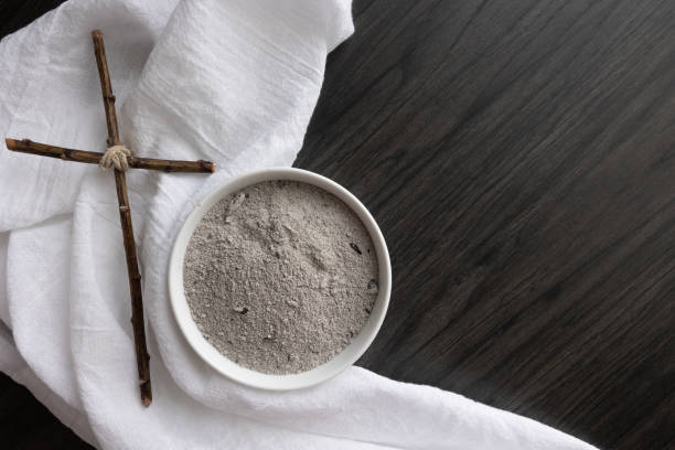 Cross, white linen and bowl of ashes on dark wood stock photo