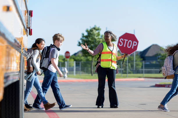 Crossing guard protects students crossing the street As students cross the street, a senior female crossing guard holds up her stop sign to traffic and protects the students. She waves to the students to keep walking. wave goodbye asian stock pictures, royalty-free photos & images