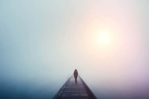 Woman crossing the bridge over lake on a foggy winter day.