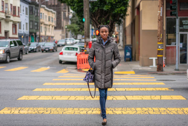 Crossing the street in San Francisco's Mission District A woman on a crosswalk during winter in San Francisco, California. approaching photos stock pictures, royalty-free photos & images