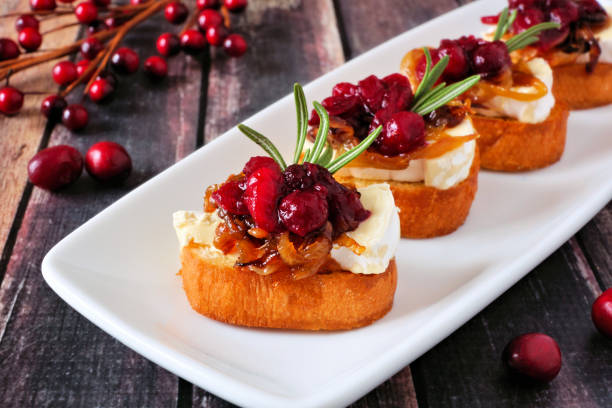 Crostini appetizers with cranberries, brie and caramelized onions on a plate against wood Crostini appetizers with cranberries, brie and caramelized onions. Close up on a serving plate against a wood background. crostini photos stock pictures, royalty-free photos & images