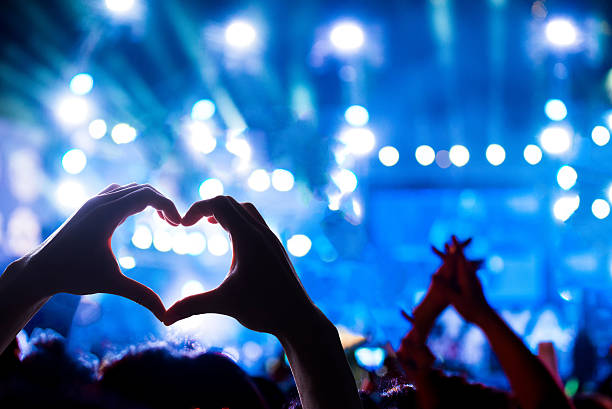 Crowd of Audience at during a concert Crowd of Audience at during a concert with silhouette of a heart shaped hands shadow, light illuminated is power of music concert opening photos stock pictures, royalty-free photos & images