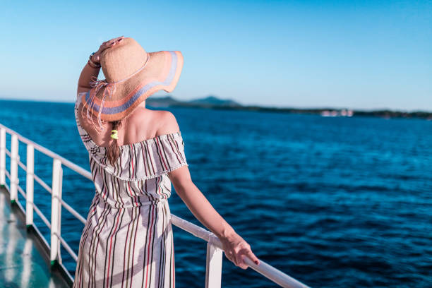 Cruise ship vacation woman enjoying travel vacation at sea. Free carefree happy girl looking at ocean and holding sunhat. stock photo