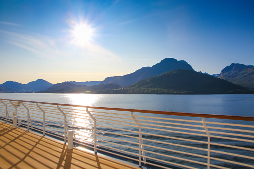 Cruise towards Geiranger fjord on a beautiful day with views of the Norweigan mountains from the open promenade deck of the ship, Norway. Sunset over the mountains with beautiful light in the landscape.