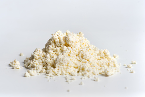 Crumbled young cow cheese pieces on a pile on white background