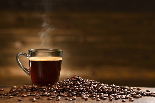 Cup glass of coffee with smoke and coffee beans on old wooden background stock photo