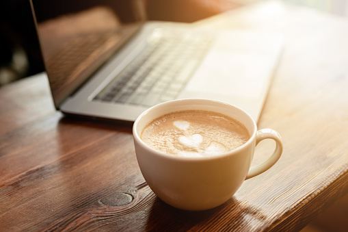 Cup of coffee cappuccino with gray laptop on wooden table. Business concept
