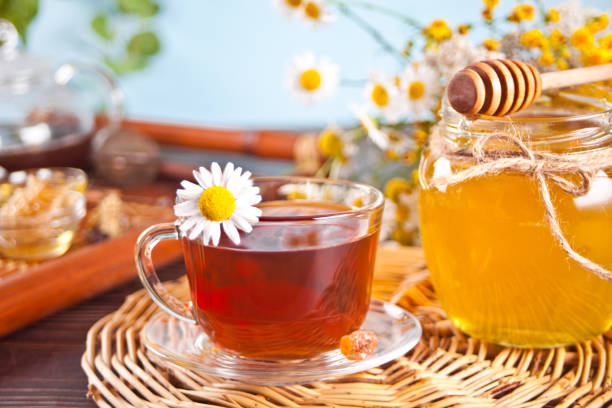 Cup of herbal tea with flowers, honey in jar, teapot and and various dried herbs on the tray. stock photo