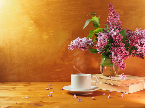A cup of hot coffee or tea on a wooden table and a vase with a bouquet of lilac
