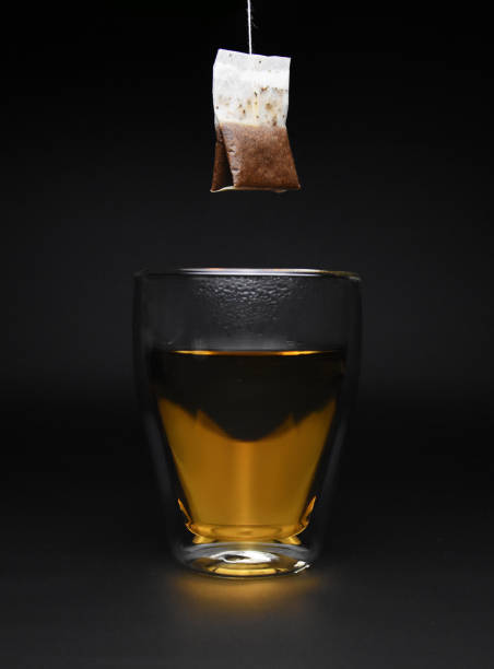 Cup of hot tea with hanging tea bag above glass isolated on black background stock photo