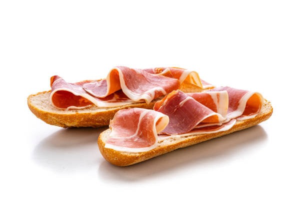 Cured Serrano ham on toast. Montadito de jamon Serrano isolated on white background Mediterranean food: Cured ham on toast isolated on white background. High resolution 42Mp studio digital capture taken with Sony A7rII and Sony FE 90mm f2.8 macro G OSS lens toasted food stock pictures, royalty-free photos & images