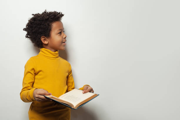 curious black child boy reading a book on white background - child reading imagens e fotografias de stock