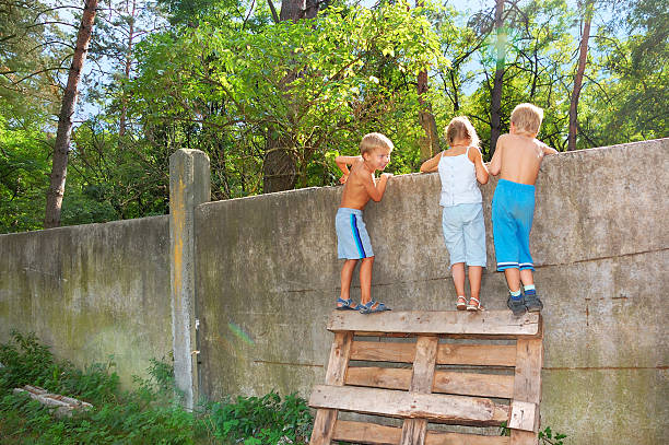 Curious children standing on a pallet to spy over the fence stock photo