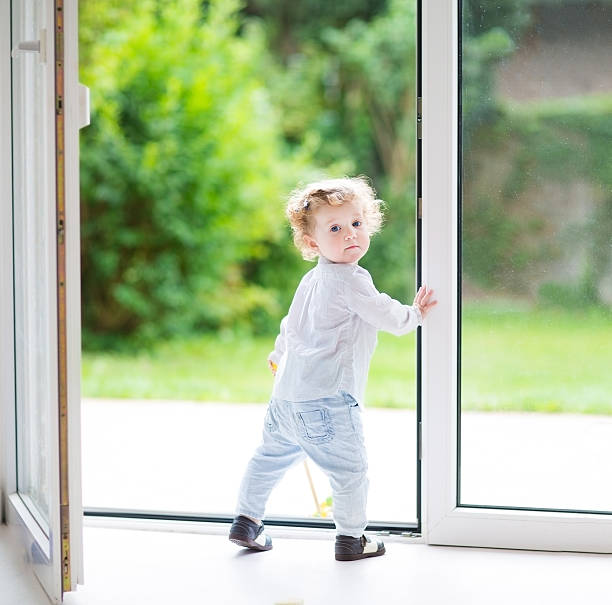 curly bebê menina em pé na grande vidro porta para jardim - family modern house window imagens e fotografias de stock