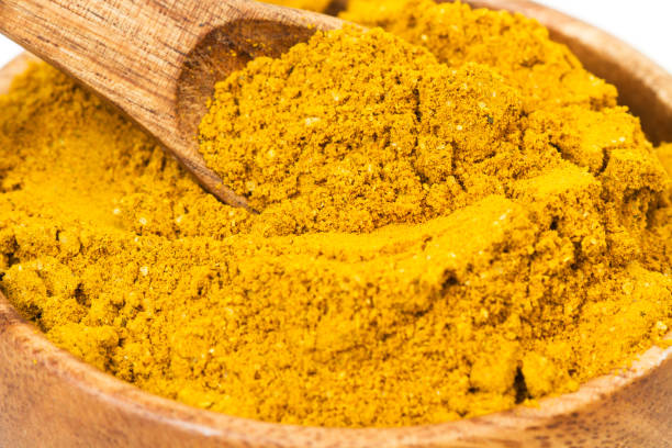 Curry powder on a wooden spoon and in a wooden bowl Curry powder on a wooden spoon and in a wooden bowl in a close up view curry powder stock pictures, royalty-free photos & images