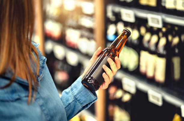 Customer buying beer in liquor store. Lager, craft or wheat beer. IPA or pale ale. Woman at alcohol shelf. Drink section and aisle in supermarket. Lady holding bottle in hand. Drink business. Customer buying beer in liquor store. Lager, craft or wheat beer. IPA or pale ale. Woman at alcohol shelf. Drink section and aisle in supermarket. Lady holding bottle in hand. Drink business concept. beer alcohol stock pictures, royalty-free photos & images