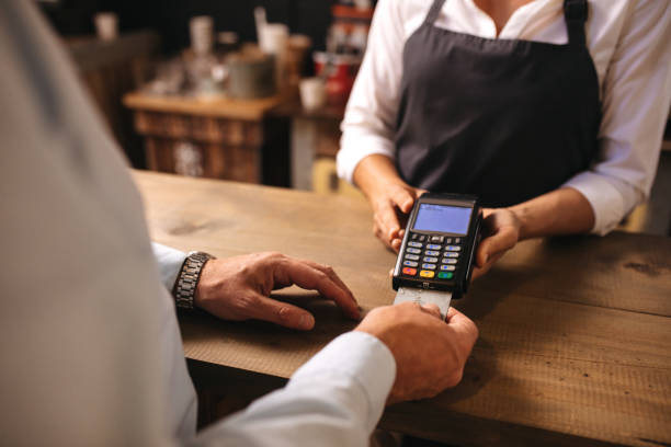 Customer doing payment of coffee by credit card at cafe Cropped shot of male customer paying for coffee by credit card at cafe. Woman barista holding a credit card reader machine with man doing payment on cafe counter. credit card reader stock pictures, royalty-free photos & images