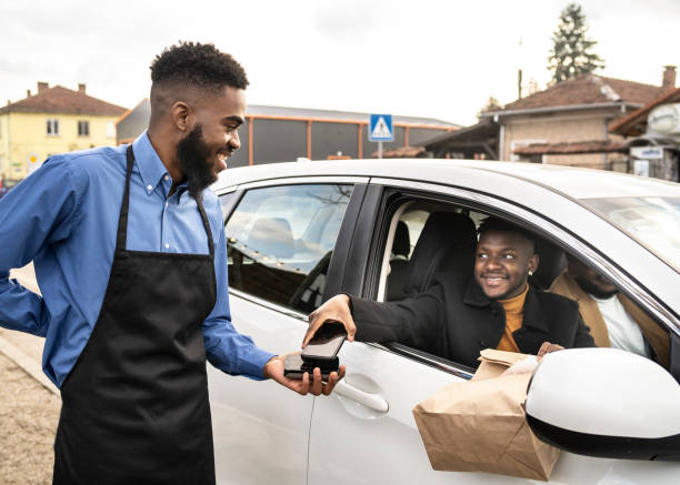 A customer paying by contactless technology while collecting his curbside delivery of take away food A customer paying by contactless technology while collecting his curbside delivery of take away food and maintaining social distance curbsidepickup stock pictures, royalty-free photos & images