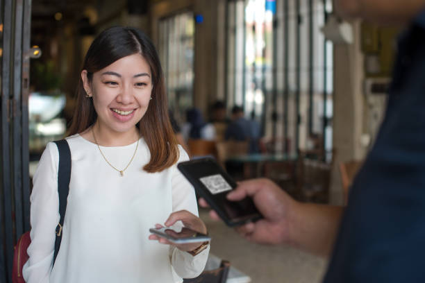 Customer scanning QR code for easy contactless payment with her smart phone at cafe Asian woman scanning QR code and paying through smart phone. Barista receiving contactless payment from customer at cafe. restaurant text marketing stock pictures, royalty-free photos & images