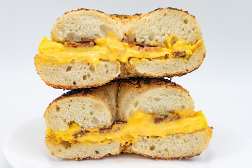 A cut in half and stacked New York style toasted sesame seed bagel filled with bacon eggs and cheese on a white plate with a white background